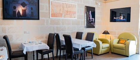 A dining area with a table set for two, a sofa, and artwork on the walls.