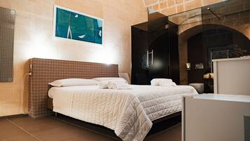 A hotel room with a large bed, a glass shower enclosure, and a stone wall.