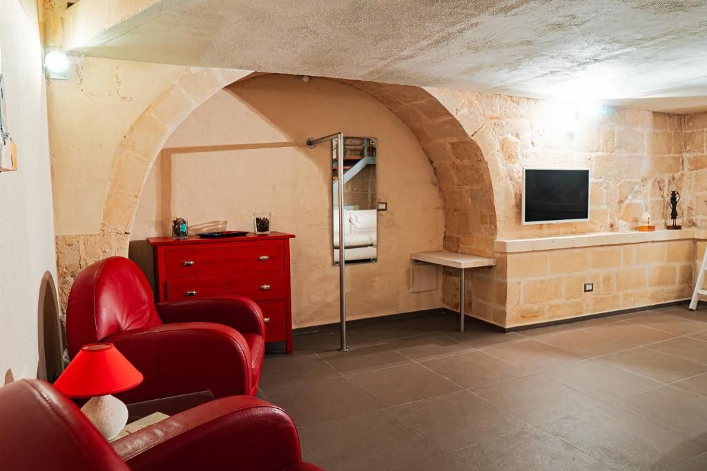 A room with a stone wall, a red chair, a small desk, and a television mounted on the wall.