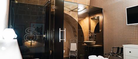 A modern hotel room with a glass-enclosed shower, a white bed, and a sink.