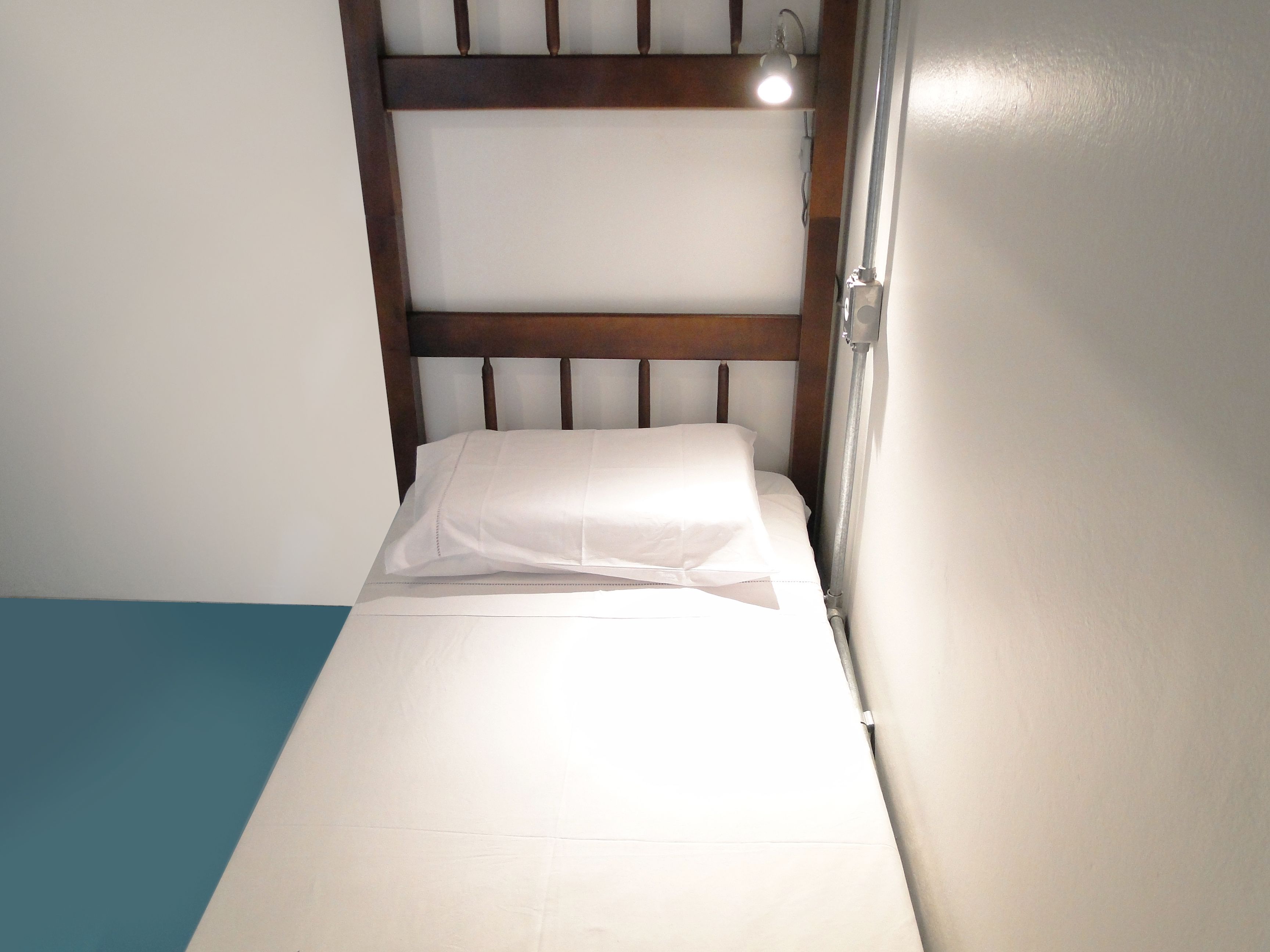 Una habitación pequeña con cama individual, cabecera de madera y lámpara de noche.