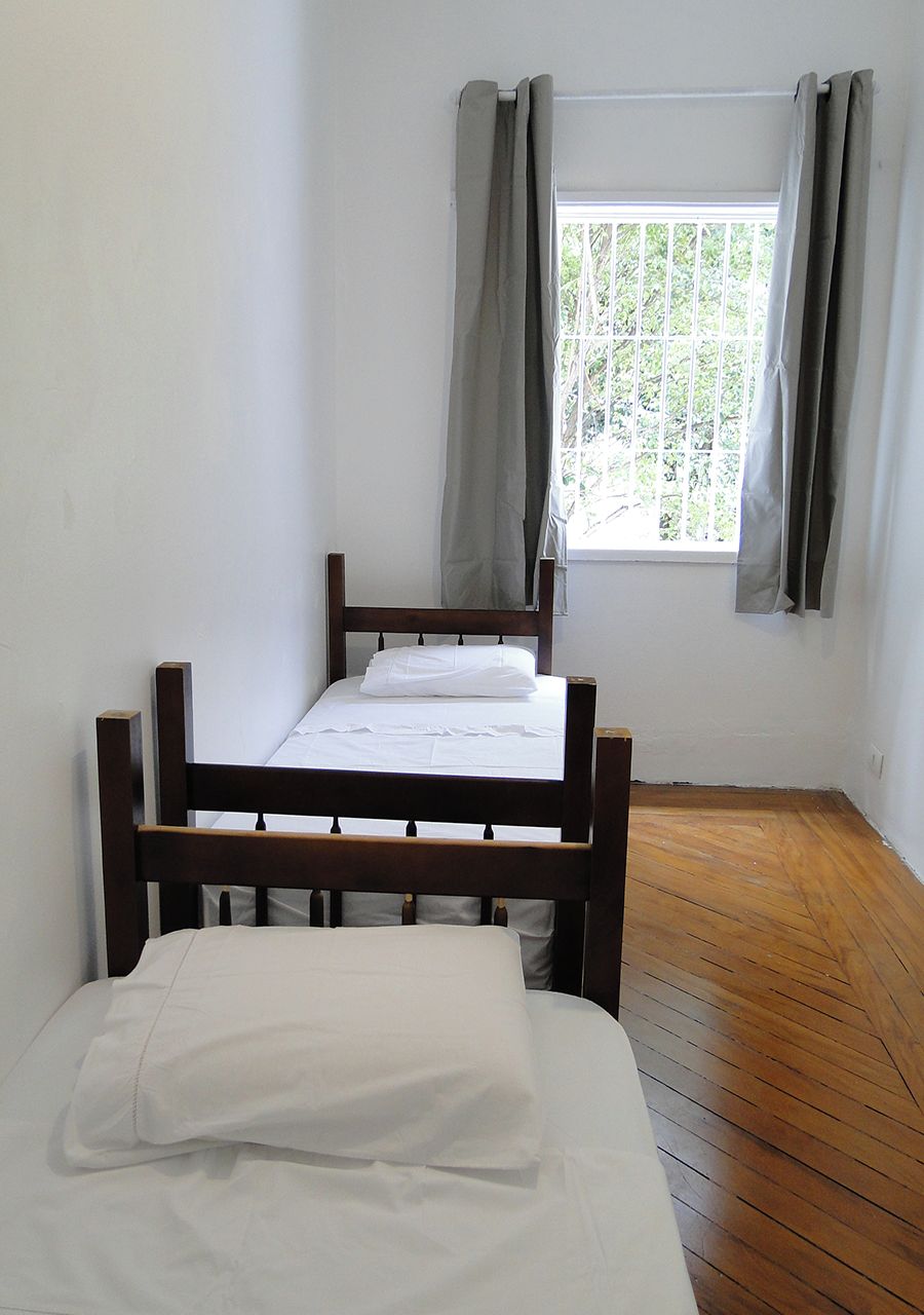 Una habitación con dos camas de madera, una ventana con cortinas y suelo de madera.
