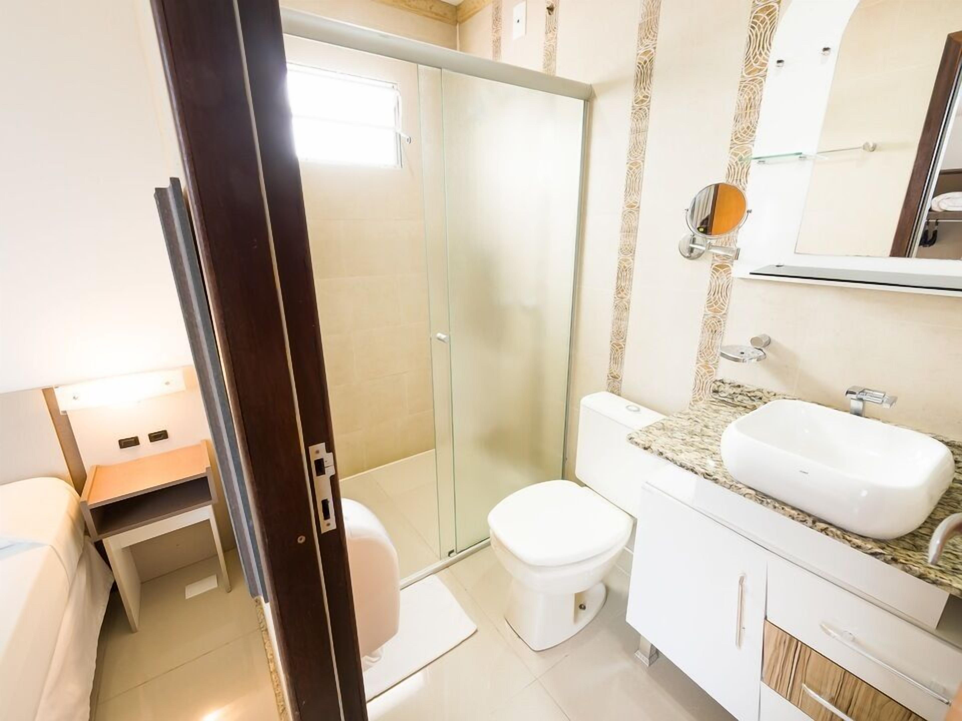 A bathroom with a glass shower enclosure, a white toilet, and a sink with a granite countertop.
