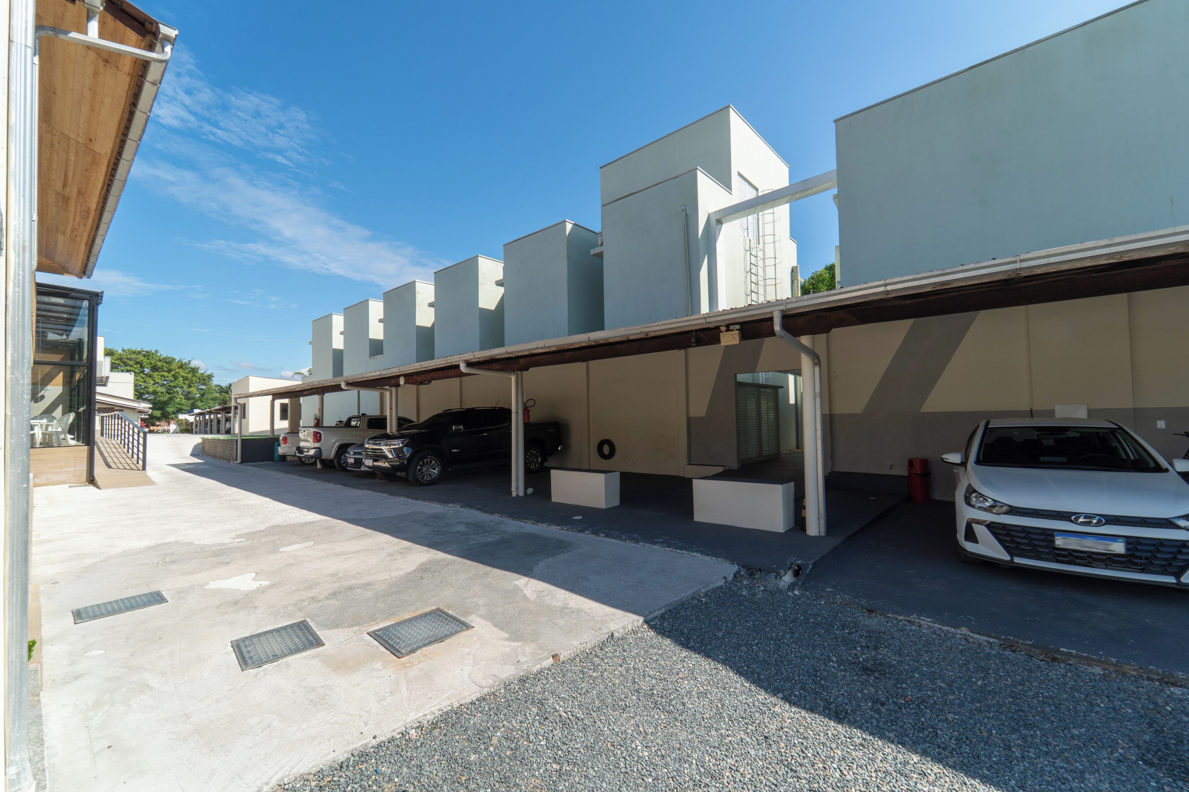 A parking area with a covered carport, a white car, and a black SUV.