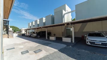 A parking area with a covered carport, a white car, and a black SUV.