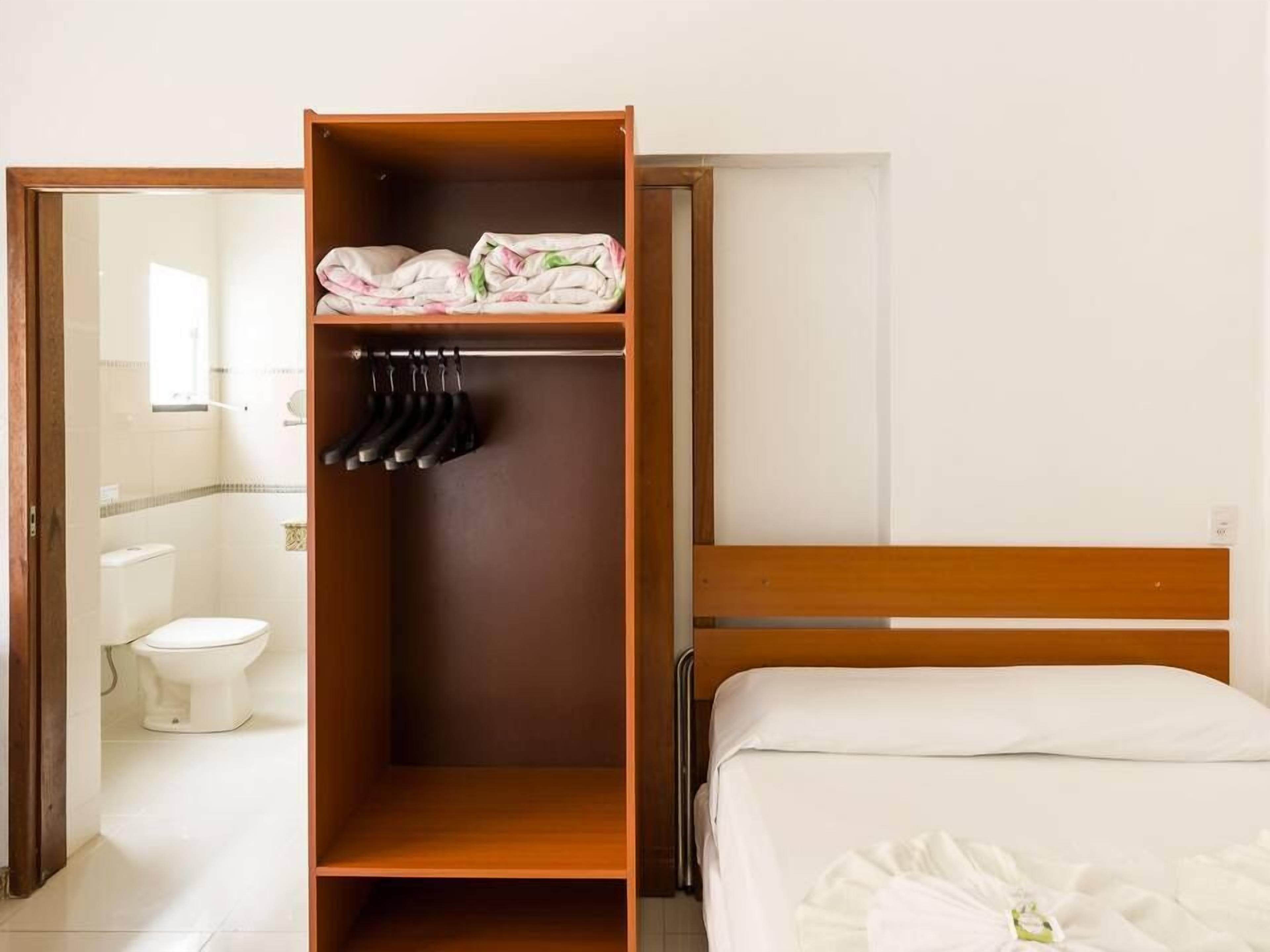 A hotel room with a wooden wardrobe, a bed with white bedding, and a bathroom visible through an open door.
