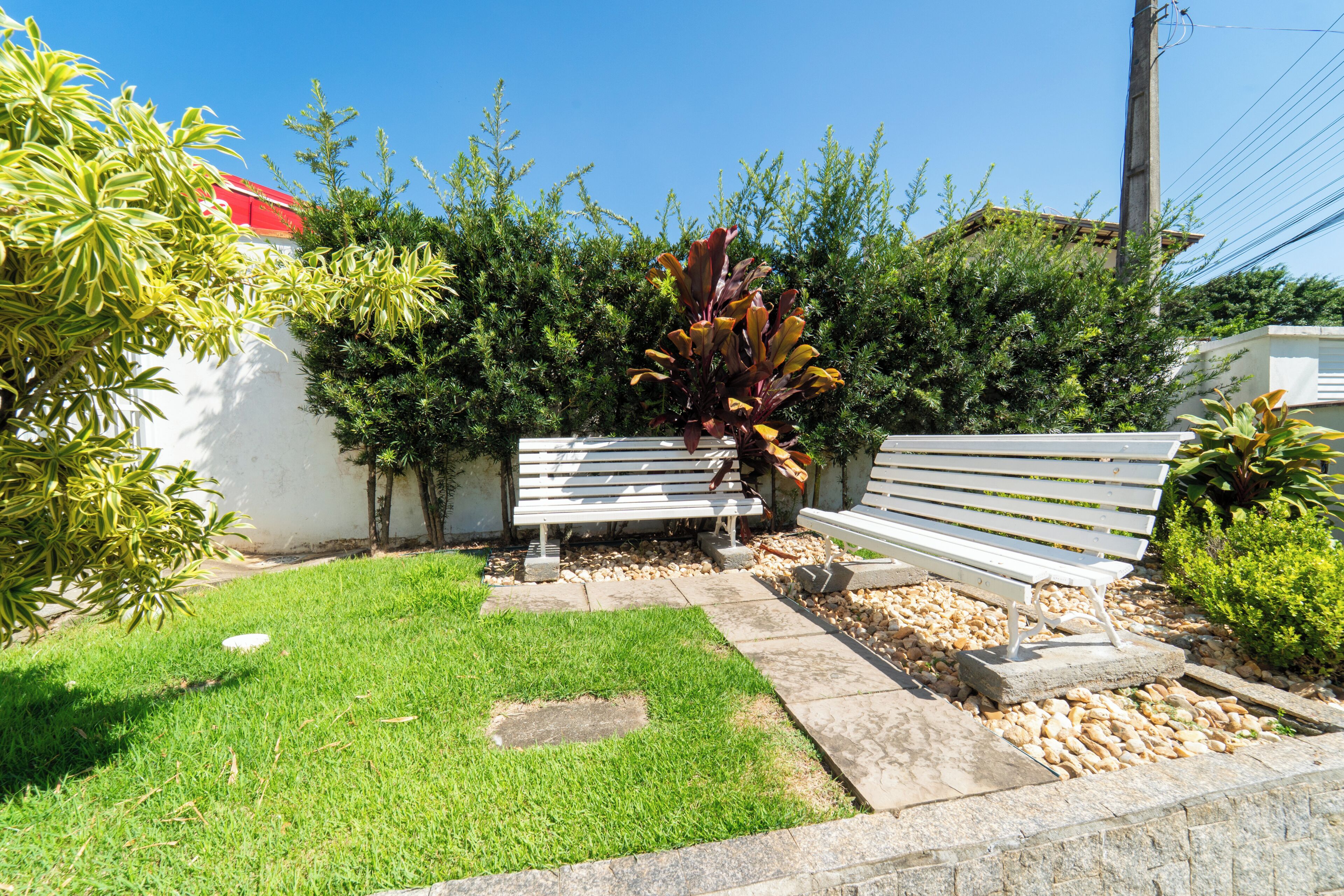 Un jardín bien cuidado con césped, un banco blanco y diversas plantas y arbustos.