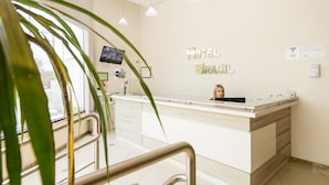 A hotel reception desk with a modern design, a television mounted on the wall, and a sign indicating the hotel name. - Hotel Brasil (Penha)