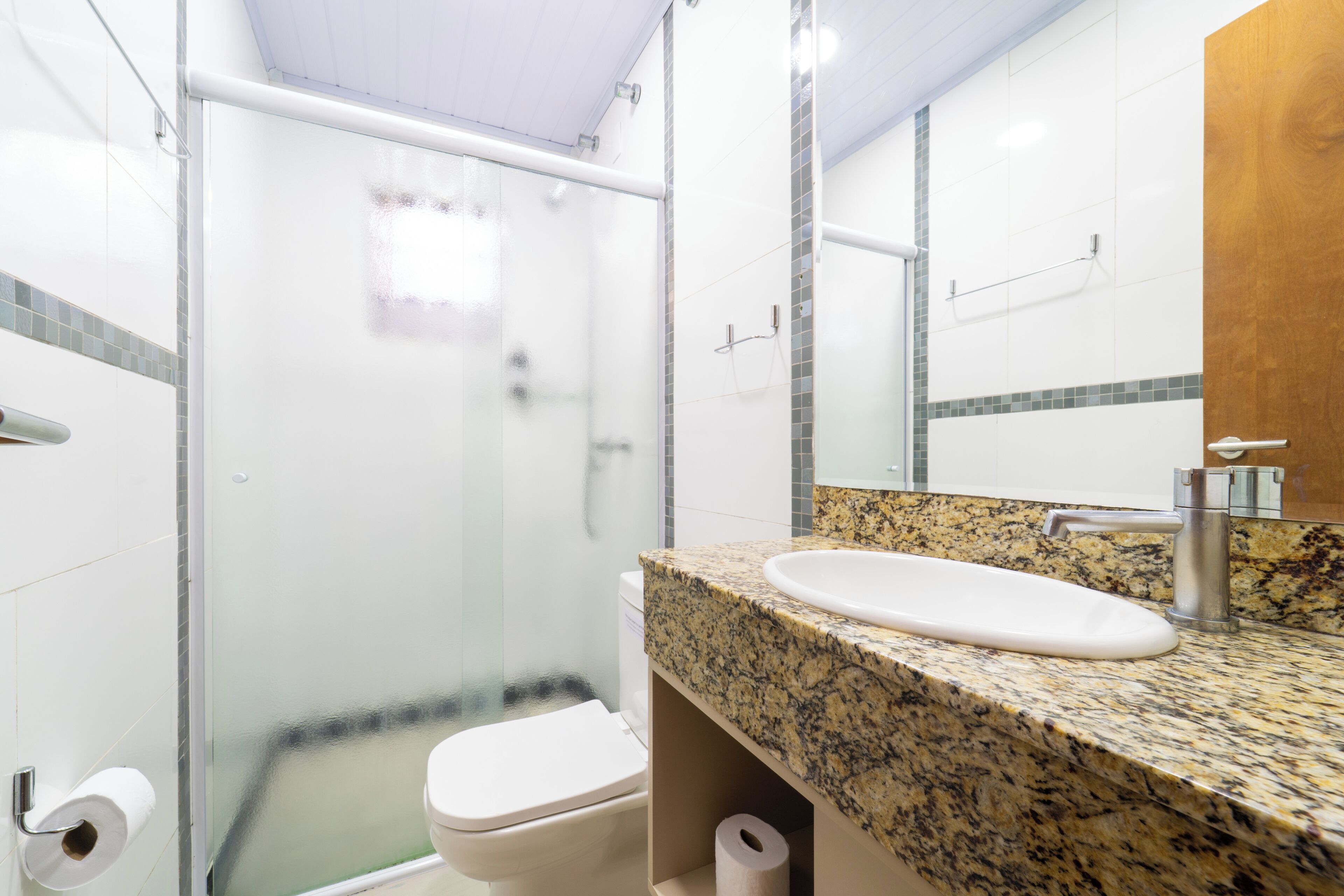 Baño con cabina de ducha de vidrio, inodoro blanco, encimera de granito y espejo.