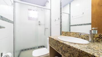 Baño con cabina de ducha de vidrio, inodoro blanco, encimera de granito y espejo.