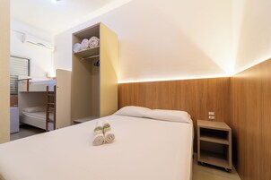 Una habitación de hotel con literas, un armario, una mesita de noche y un pequeño estante.