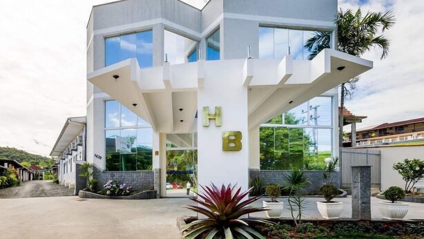 A modern multi-story building with large windows and a prominent 'H' and 'B' sign, surrounded by well-maintained landscaping. - Hotel Brasil (Penha)