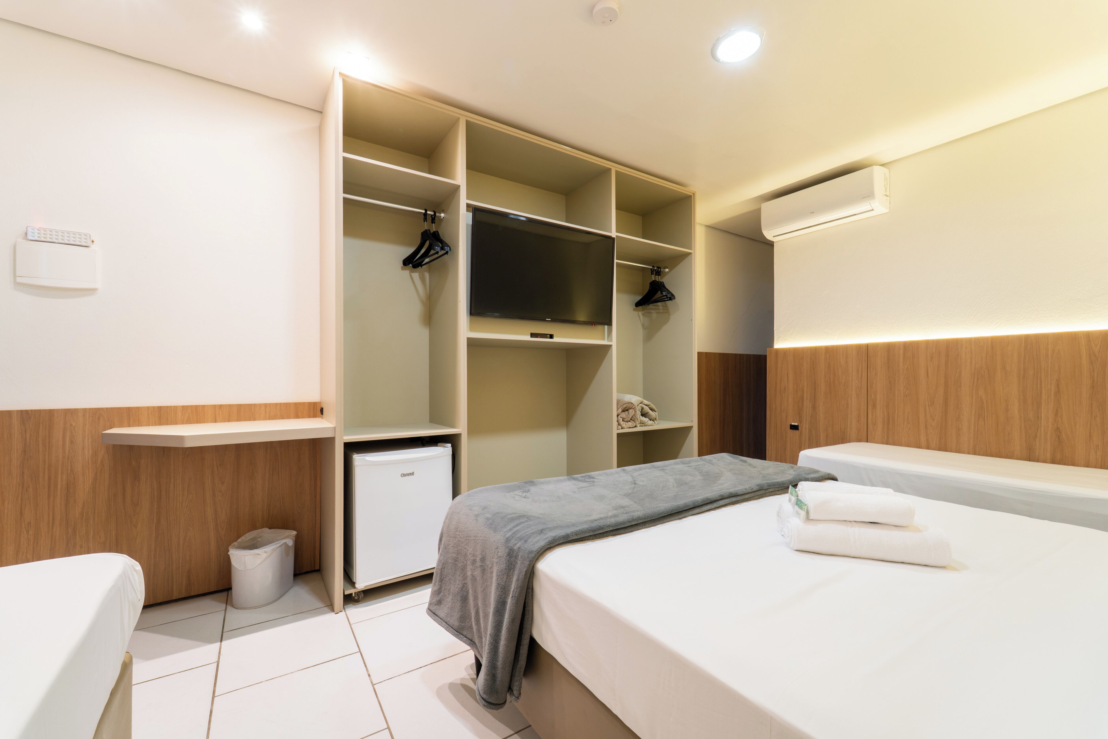 Habitación de hotel con cama, mesita de noche, armario con espacio para colgar y un cubo de basura.