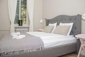 Uma cama bem arrumada com um cobertor listrado, uma mesinha de cabeceira com abajur e uma janela com cortinas.