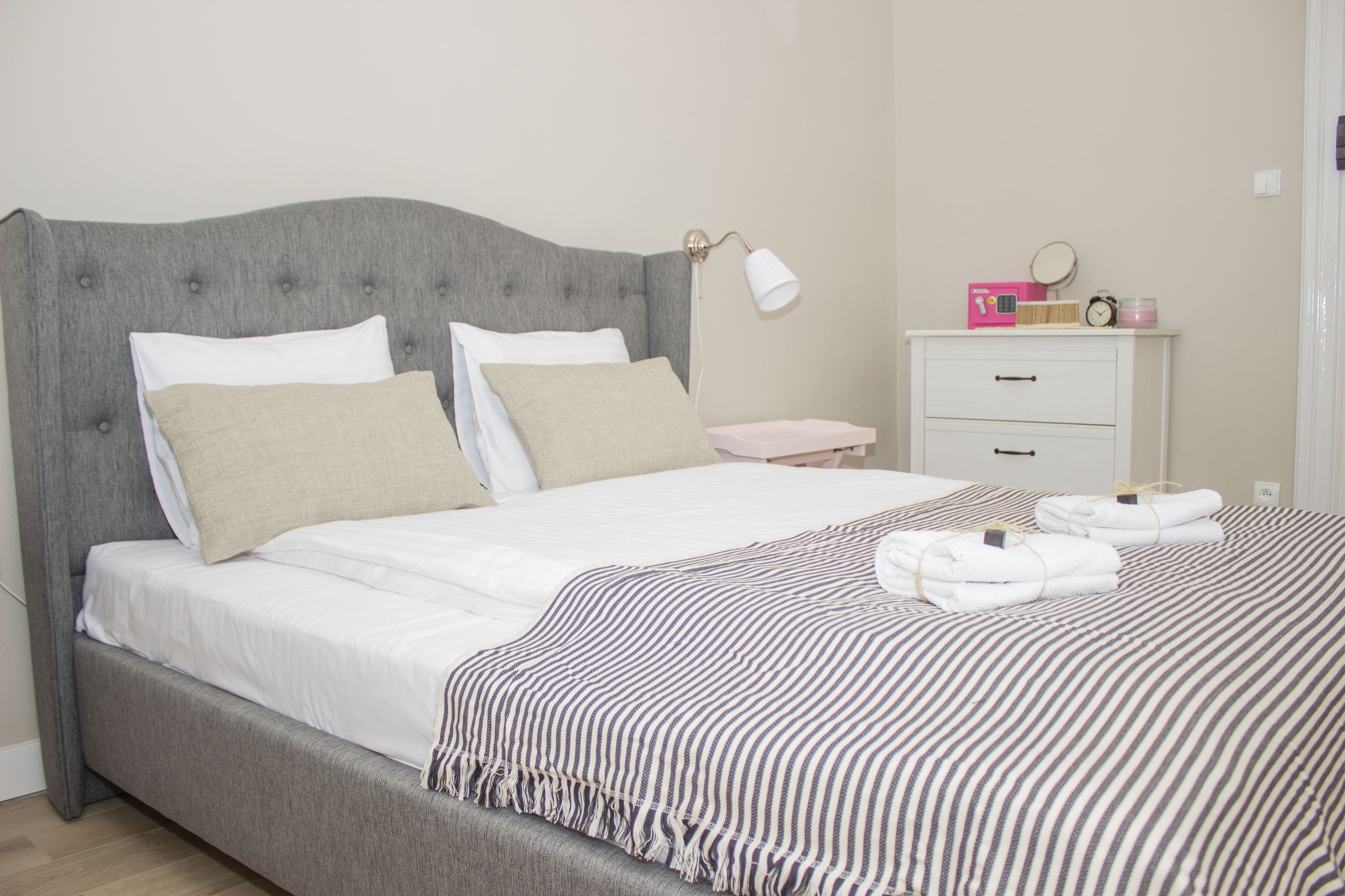 A neatly made bed with a striped blanket, a bedside table with a lamp, and a small cabinet with toiletries.