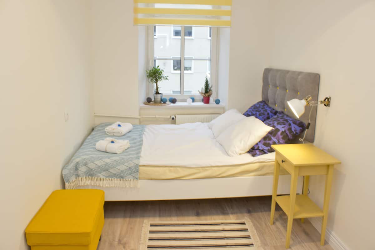 Une chambre bien rangée, avec un lit, une table de chevet et une fenêtre agrémentée de plantes.