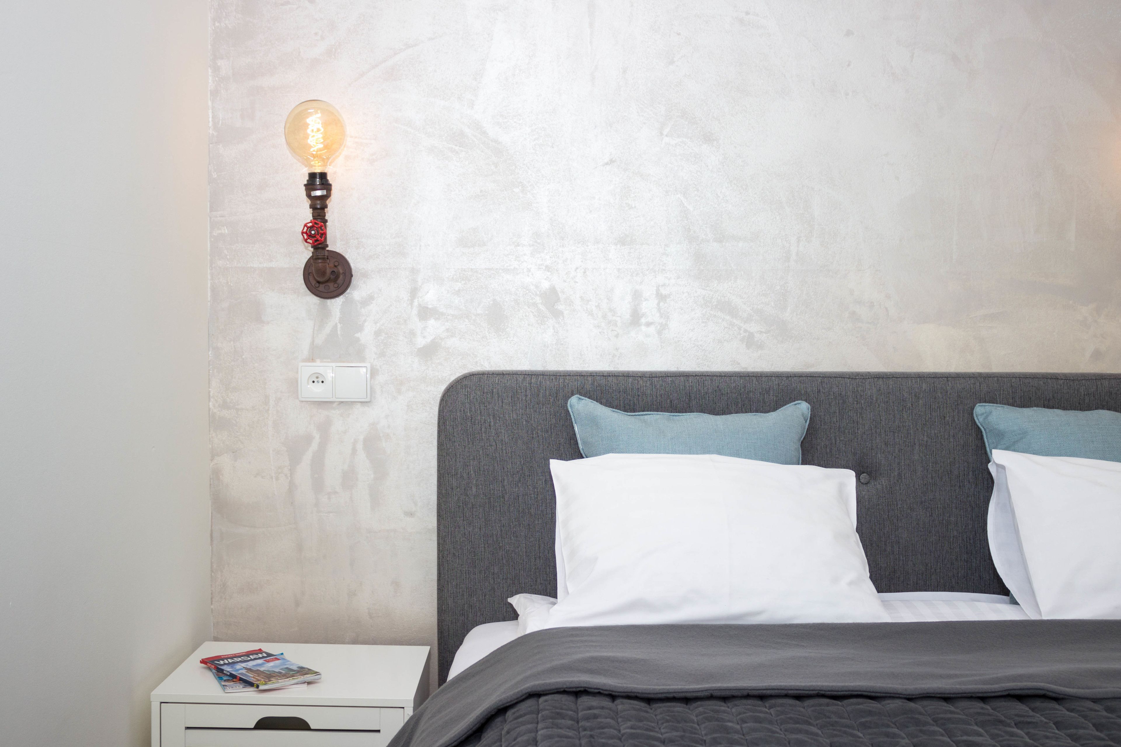 A bedroom with a bed, pillows, a nightstand, a lamp, and a magazine.