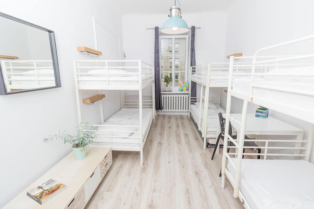 Une chambre avec des lits superposés, un bureau, une chaise, une plante en pot et une fenêtre avec des rideaux.
