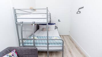 A bunk bed with a lower bunk, a grey couch with a colorful pillow, and a door with a coat hanger.