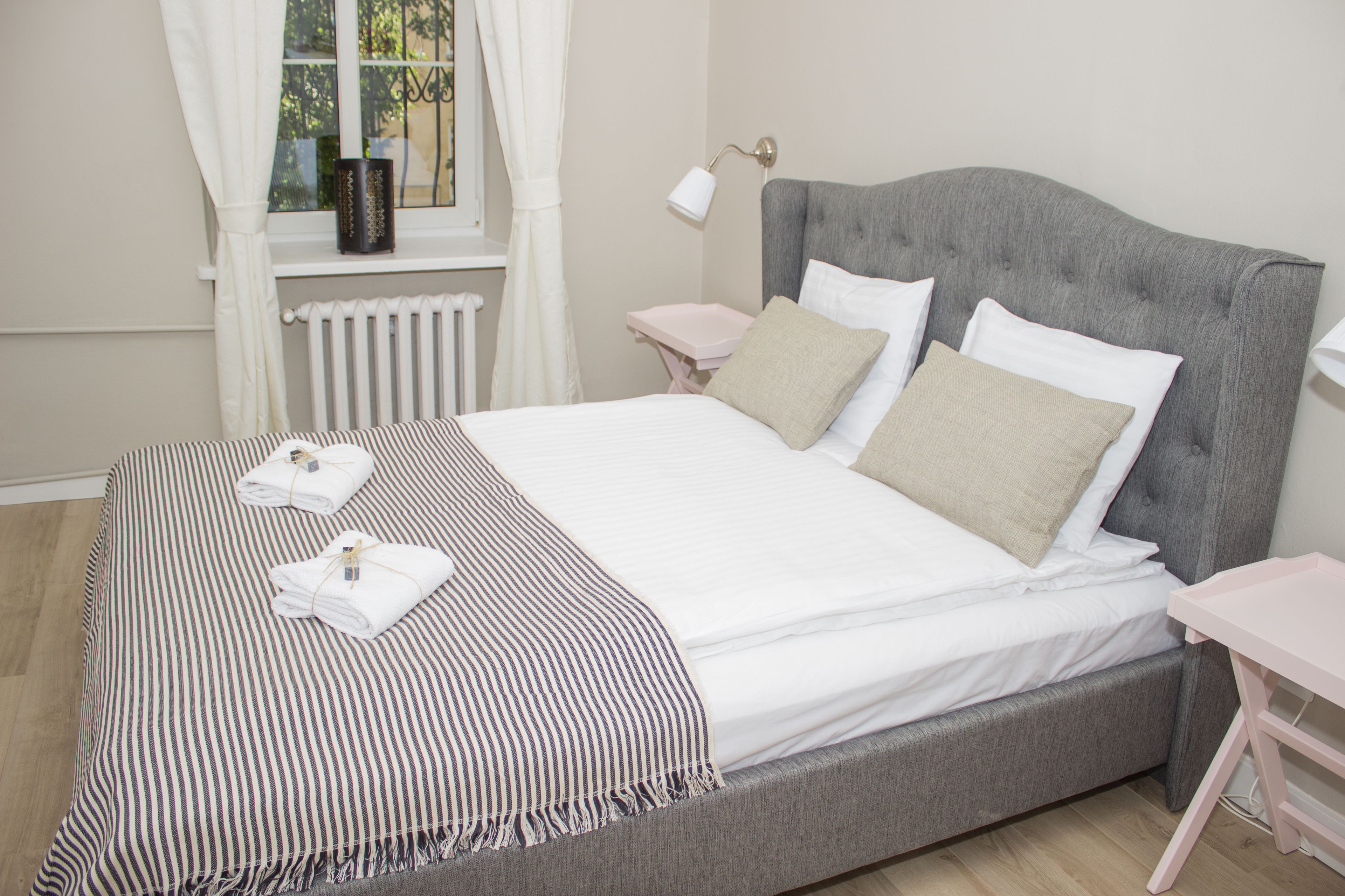 A neatly made bed with a striped blanket and pillows, a bedside table with a lamp, and a window with curtains.