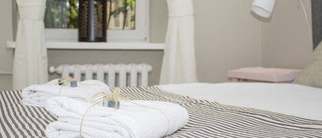 A neatly made bed with striped bedding, a bedside lamp, and a window with curtains.