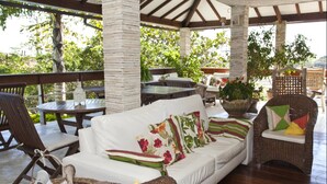 A covered outdoor seating area with a white sofa, wicker chairs, and a table. - Bon Bini Pousada (Búzios)
