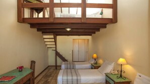 A dormitory-style room with two beds, a wooden loft above, a desk, and a staircase leading to another room. - Bon Bini Pousada (Búzios)