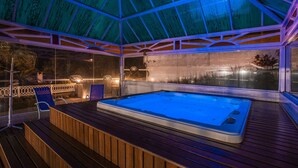 A hot tub under a glass roof with wooden decking and chairs. - Pousada das Videiras (Camanducaia)