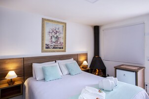 Una habitación de hotel con cama, lámparas de noche, un cuadro, un calentador y un minibar.