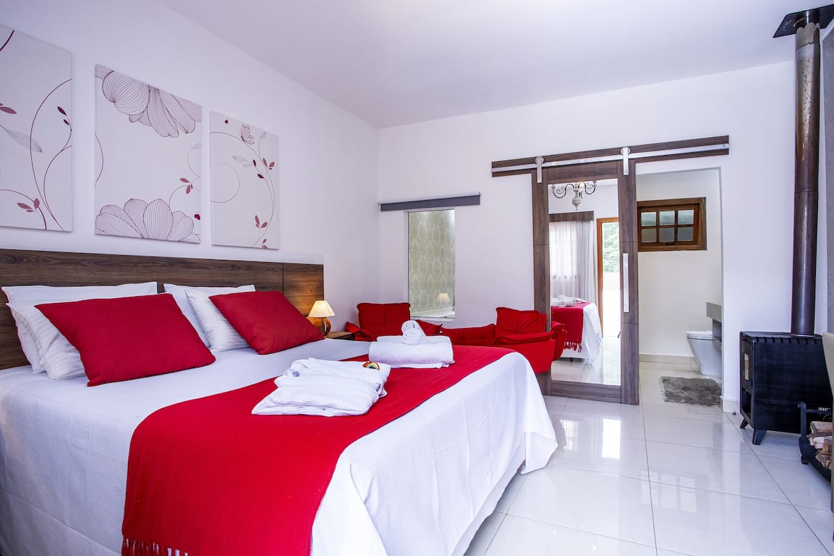 Una habitación de hotel moderna con una cama grande, ropa de cama roja y blanca, un cabecero de madera y un ventanal amplio.