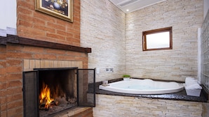 A bathroom with a brick fireplace, a freestanding bathtub, and a framed picture on the wall. - Pousada das Videiras (Camanducaia)