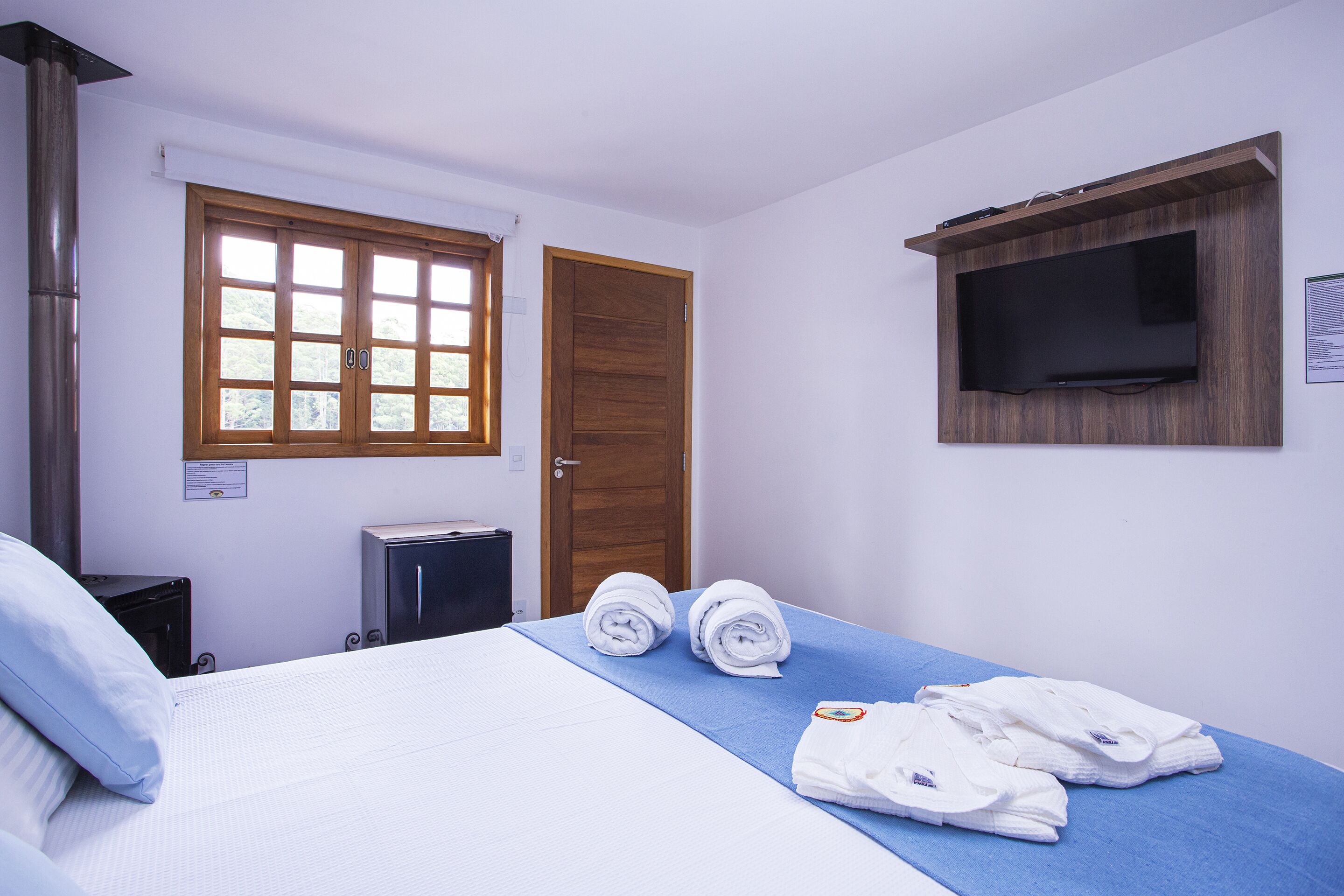 A hotel room with a bed, a TV mounted on the wall, a window, and a door.