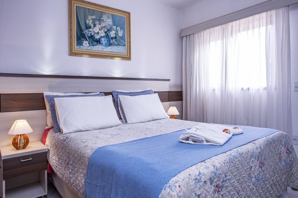Una cama bien hecha con una colcha azul, almohadas blancas y una toalla doblada sobre la cama.