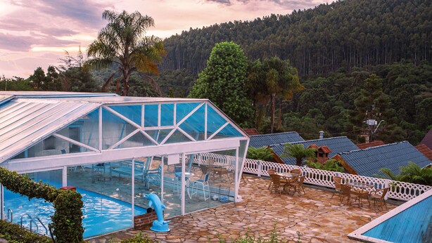 A pool area with a glass enclosure, outdoor seating, and a view of a forested hillside. - Pousada das Videiras (Camanducaia)