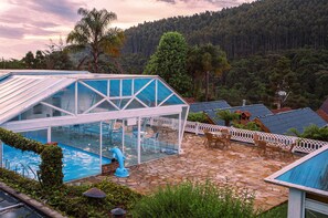 Un área de piscina con cerramiento de vidrio, mobiliario exterior y vistas a una ladera boscosa.