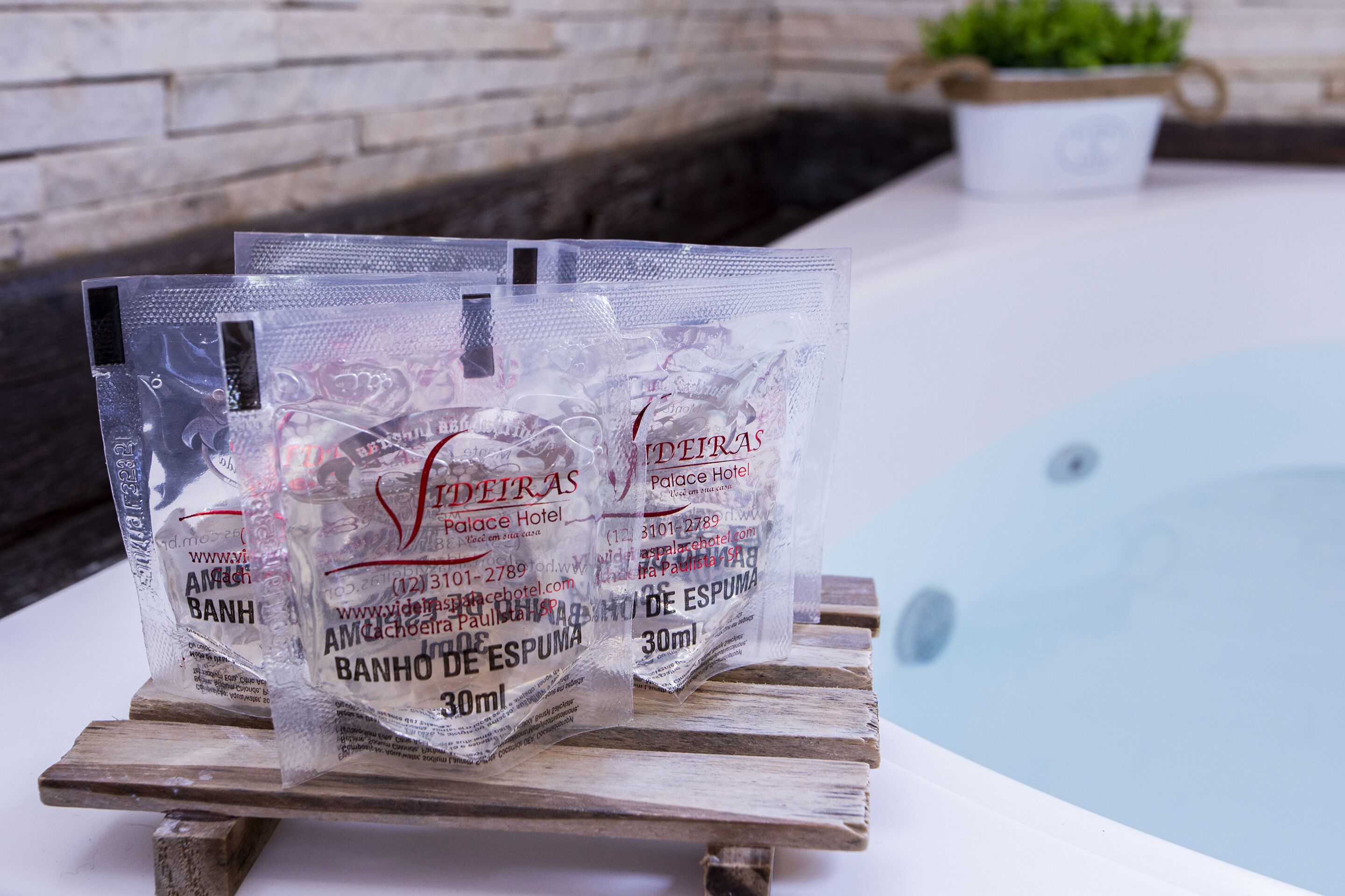 Sacchetti di plastica con l'etichetta 'BANHO DE ESPUMA' e capacità di 30ml, posizionati su un piano di legno vicino a una piscina.