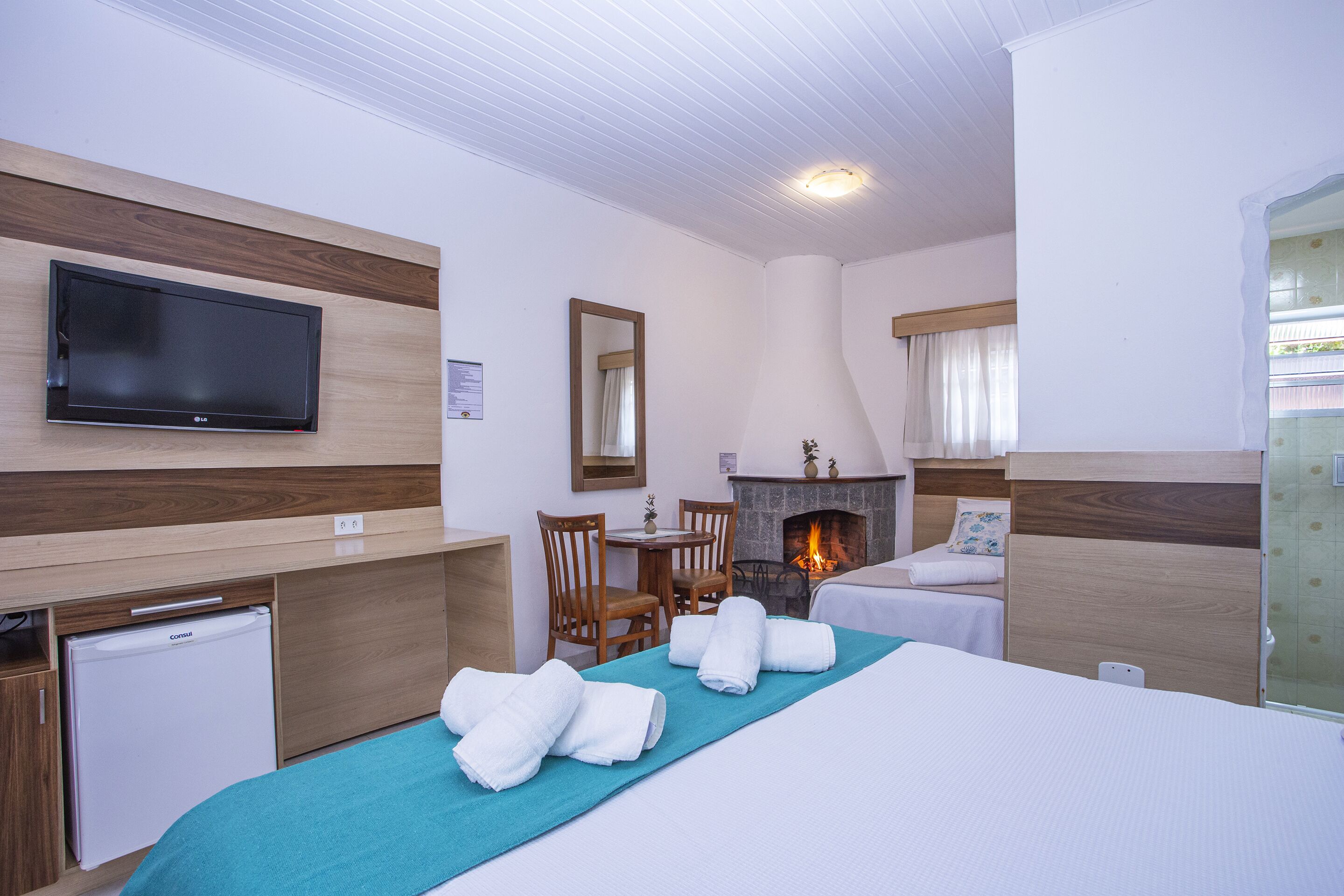 Een hotelkamer met een flatscreen-tv, een open haard, een bed met handdoeken, een bureau met een koelkast en een zithoek met stoelen.