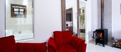 Una sala moderna con dos sillones rojos, una puerta de vidrio que da a un baño y una estufa de leña.