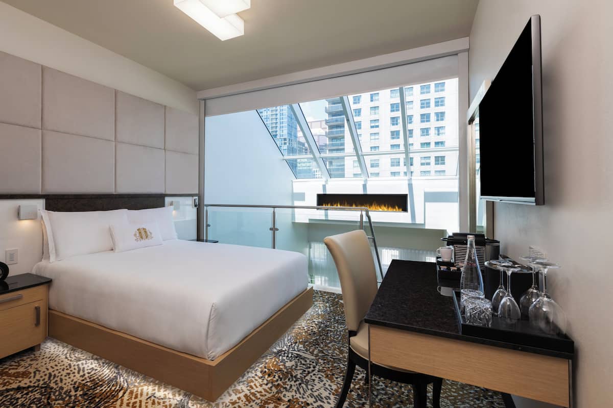 Habitación de hotel con cama, escritorio, silla, televisor, chimenea y vistas a edificios.