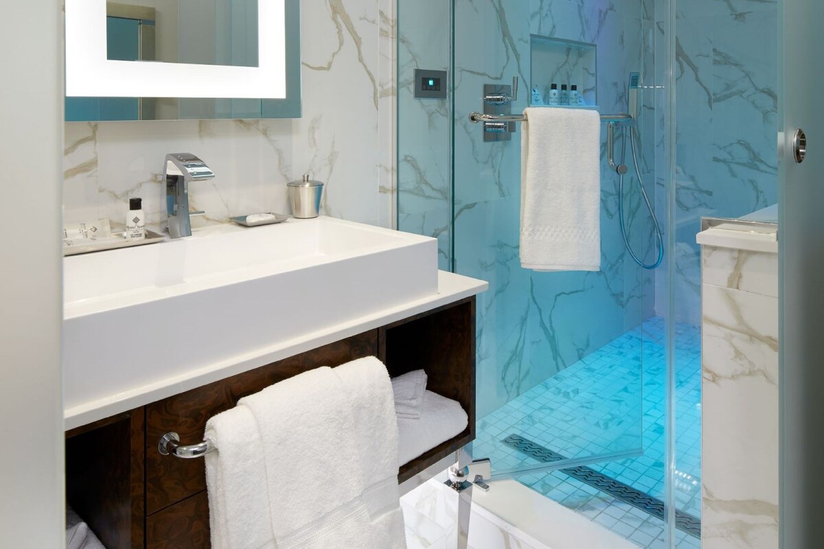 A modern bathroom with a glass-enclosed shower, a marble-tiled floor, and a white sink with a mirror above it.