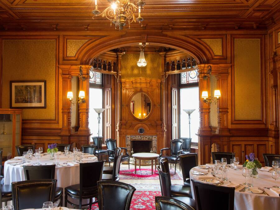 A formal dining room with multiple tables set for a meal, wooden paneling, and a large mirror.