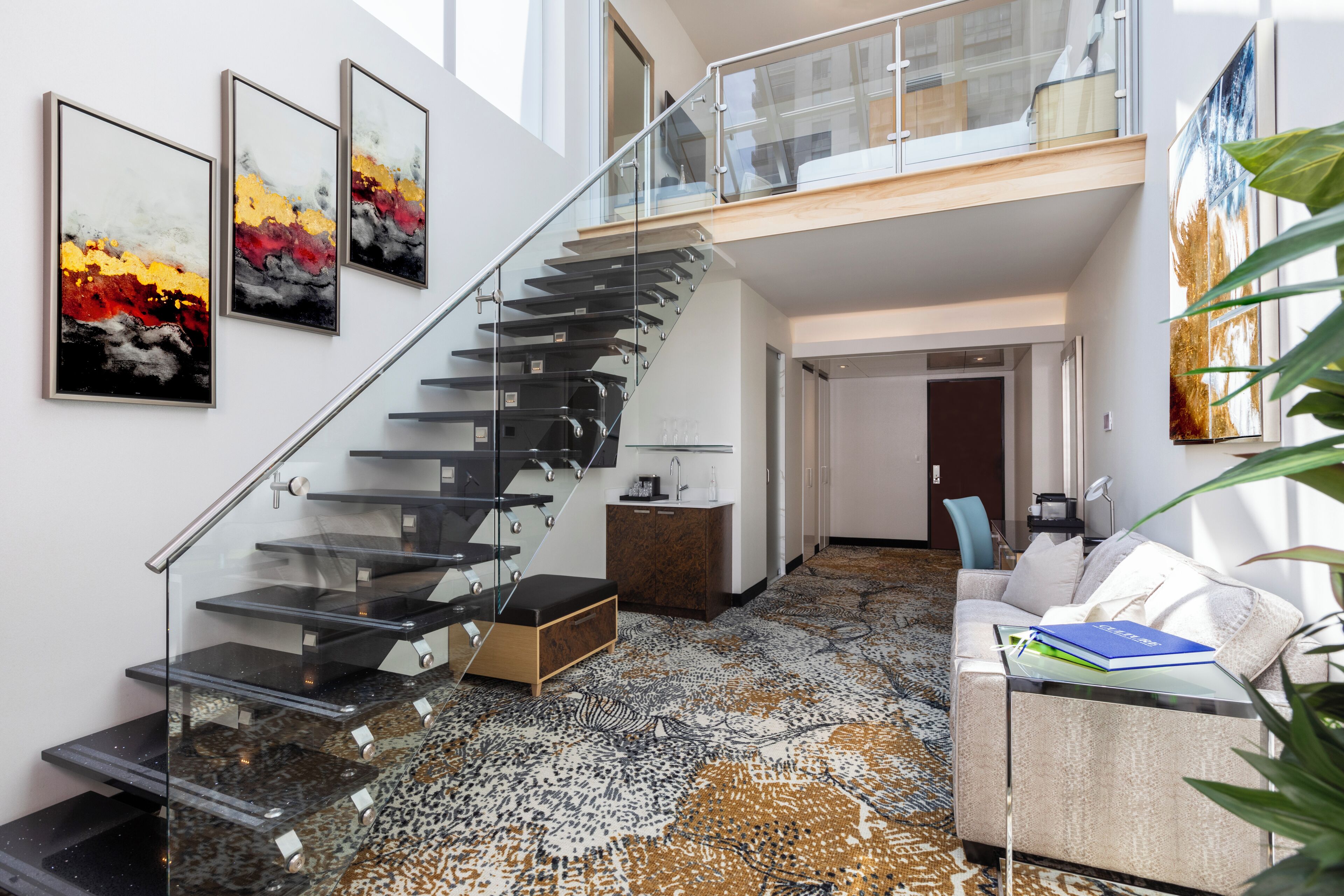 A modern interior with a glass staircase, a patterned carpet, a white sofa, and artwork on the walls.