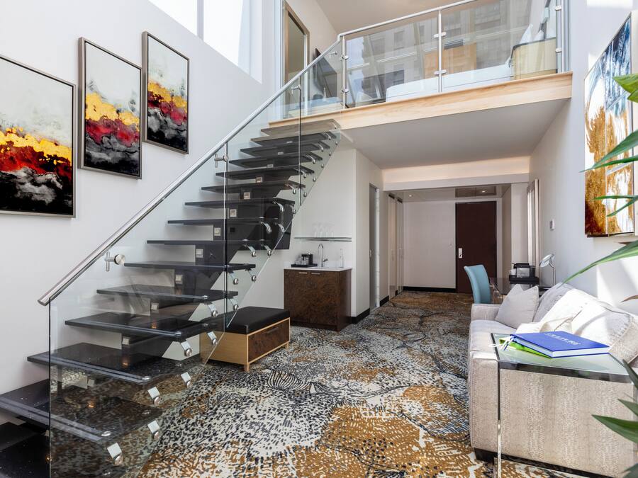 A modern interior with a glass staircase, a patterned carpet, a white sofa, and artwork on the walls.