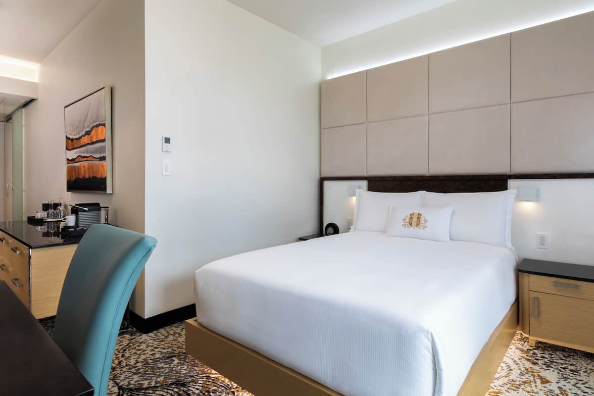 Una habitación de hotel con una cama grande, mesitas de noche, un escritorio con silla y un cuadro en la pared.