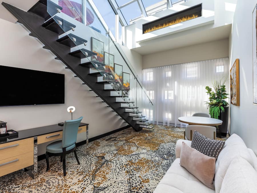 Una sala de estar moderna con una escalera, un televisor de pantalla plana, un escritorio y un sofá.