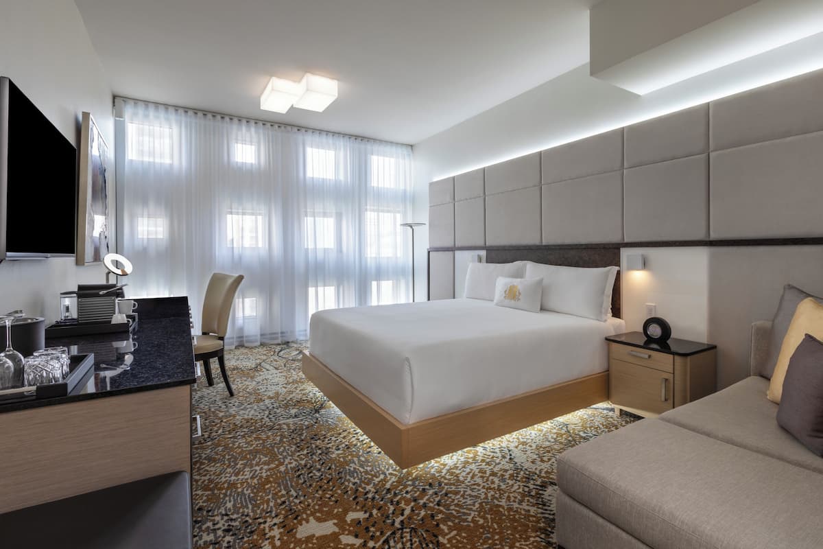 Una habitación de hotel moderna con una cama grande, mesitas de noche, un escritorio con silla, un televisor de pantalla plana y una alfombra estampada.