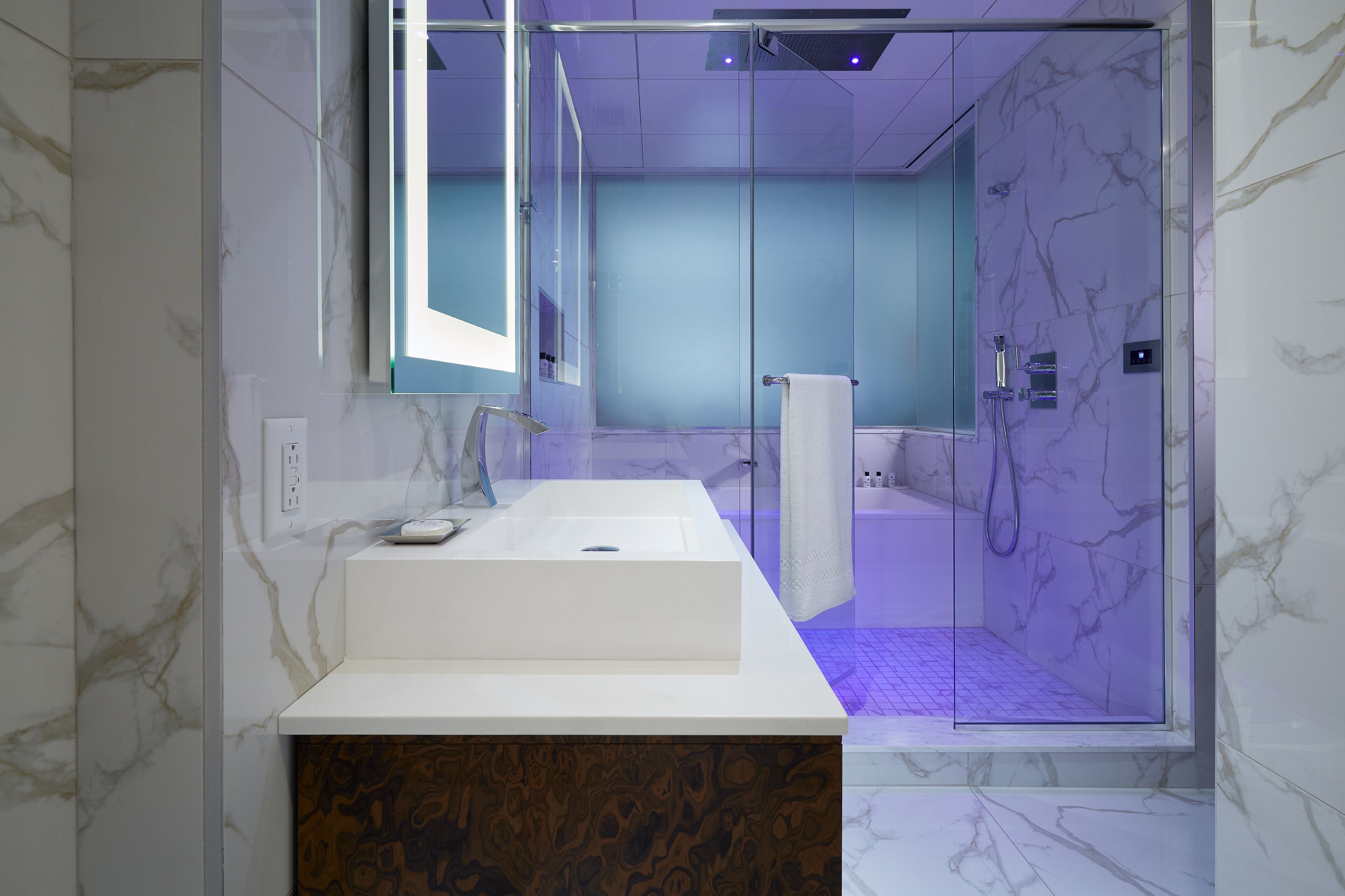 Ein modernes Badezimmer mit Waschbecken aus Marmor, einer Duschkabine aus Glas und einem großen Spiegel.
