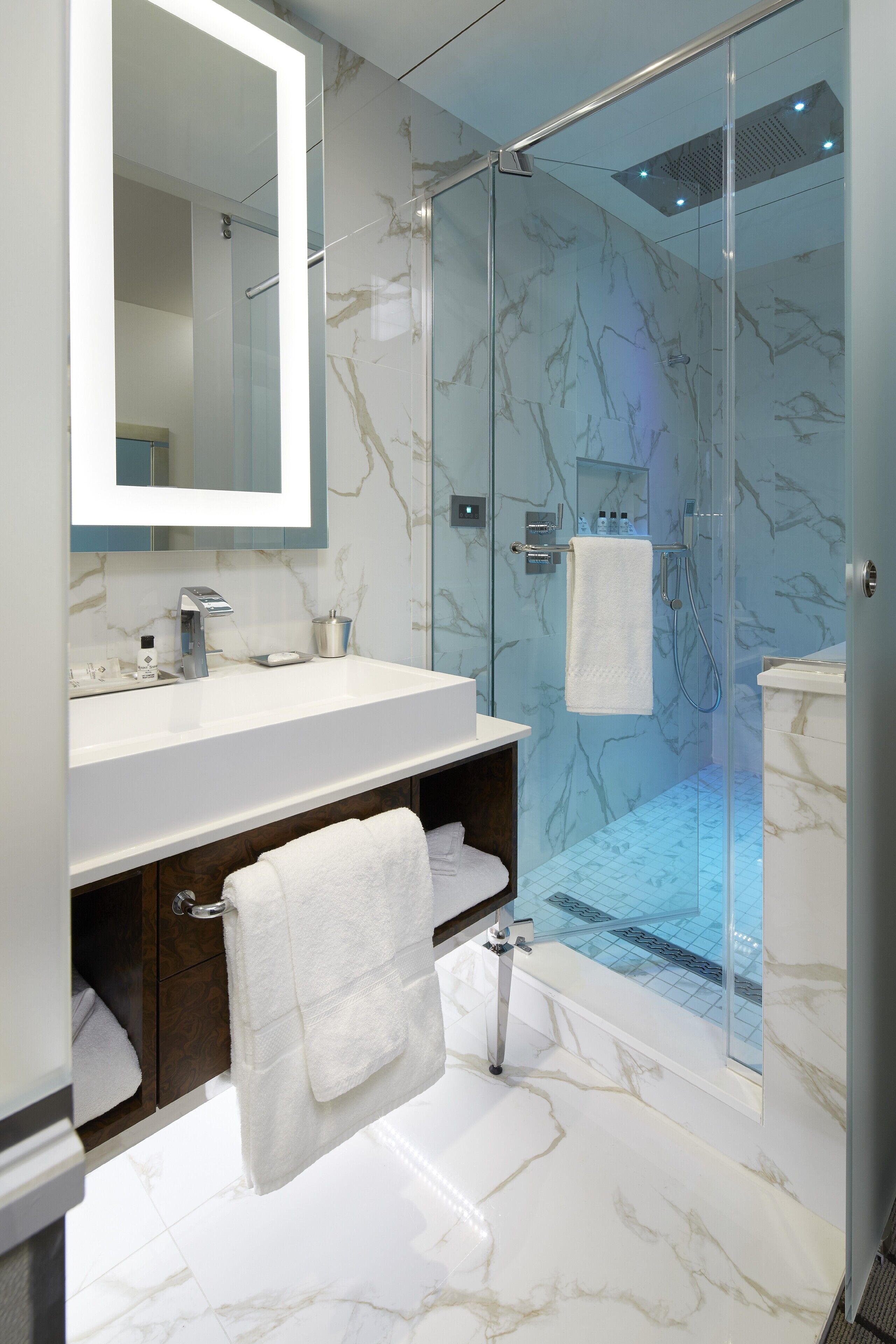 A modern bathroom with a glass-enclosed shower, marble flooring, and a large mirror above the sink.
