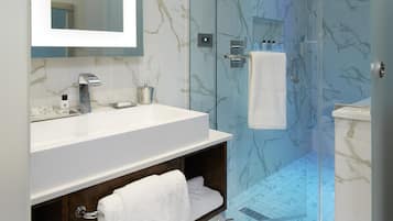 A modern bathroom with a glass-enclosed shower, marble flooring, and a large mirror above the sink.