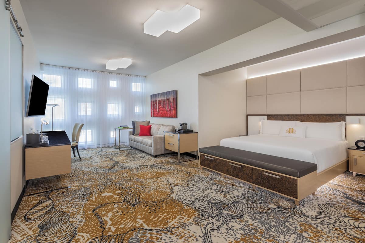 Habitación de hotel con cama, escritorio, silla, televisor y un cuadro en la pared.
